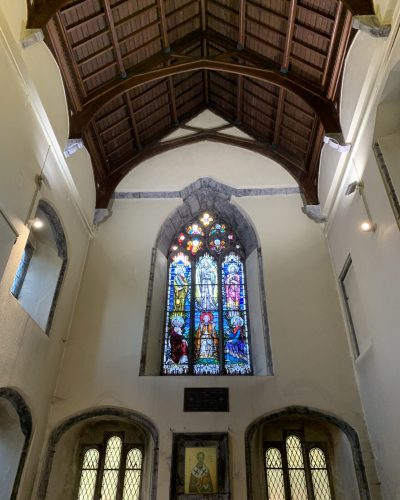 A church interior with a high wooden ceiling, stained glass windows depicting religious figures, and arched stone details. Discover its rich history and architecture on a Galway Guided Tour, highlighting icons and intricate lattice windows.